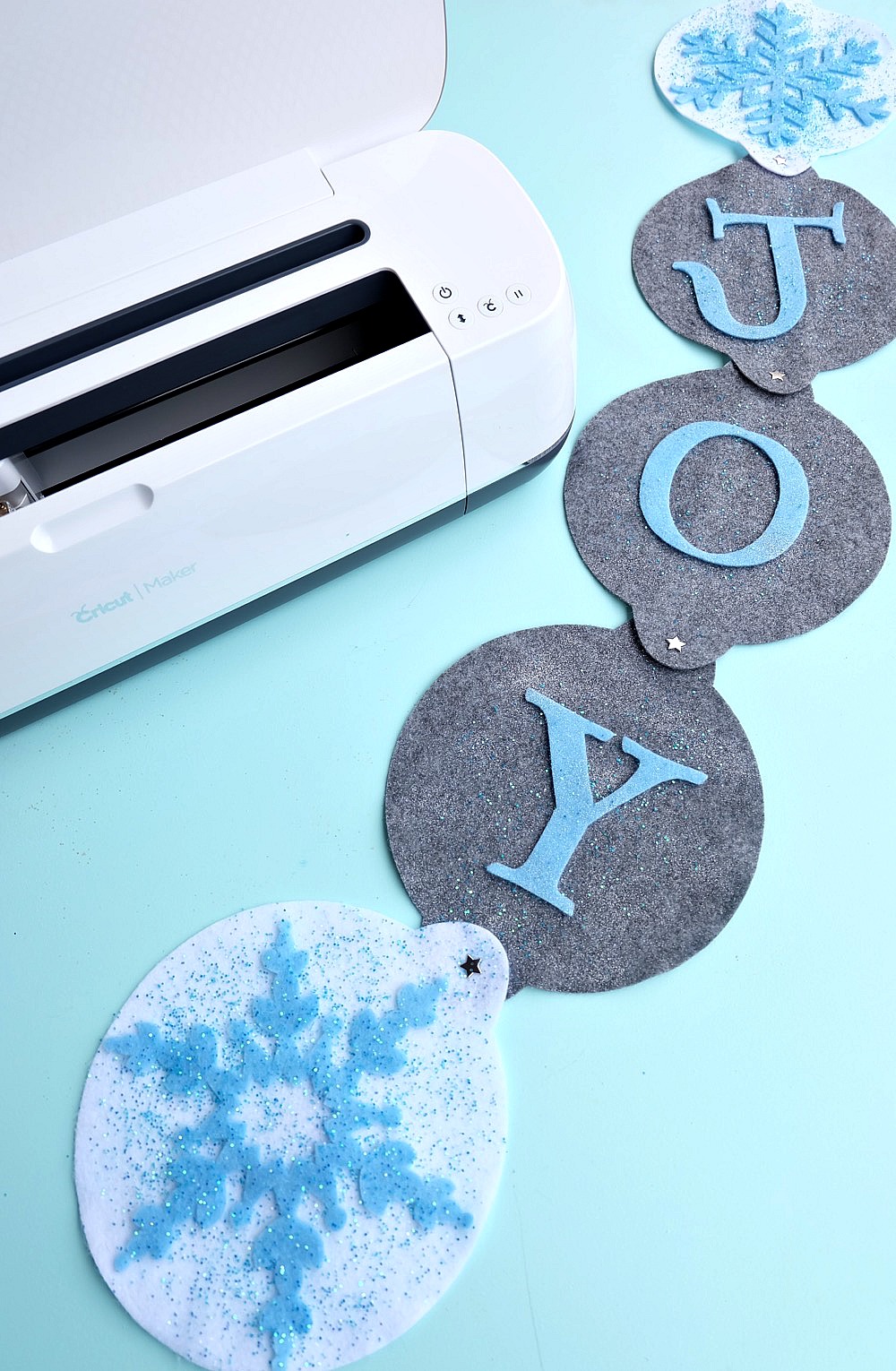 The new Cricut Maker cuts felt like butter! Learn how to make this DIY "Joy" Felt Winter Door Decoration in this no sew project that's perfect for a front door Christmas wreath substitute! How pretty are the sparkle snowflakes? #CricutMade #CricutHoliday #ChristmasCrafts #sponsored