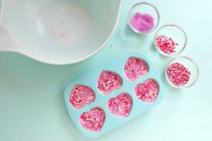 Add more candy sprinkles to the top of your bath bombs. Press firmly so the candies are embedded in the bath bombs. If you are worried about the candies sticking on top you can pour a bit of coconut oil on top and press down with a spoon to seal them in.