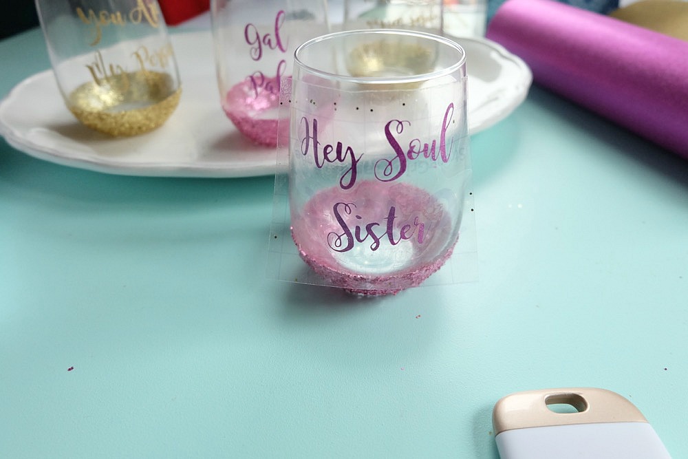 Celebrate Galentine's Day (aka Valentine's Day for with your BFF's) with these super cute DIY Glitter Dipped Wine Glasses. This post shares word art to make 6 different glasses along with an easy step by step tutorial with photos for how to make this project. This would be a great crafternoon project with friends! Use your Cricut to cut the word art. #CricutMade #Crafts #Galentine #DIY #Glitter #Valentine