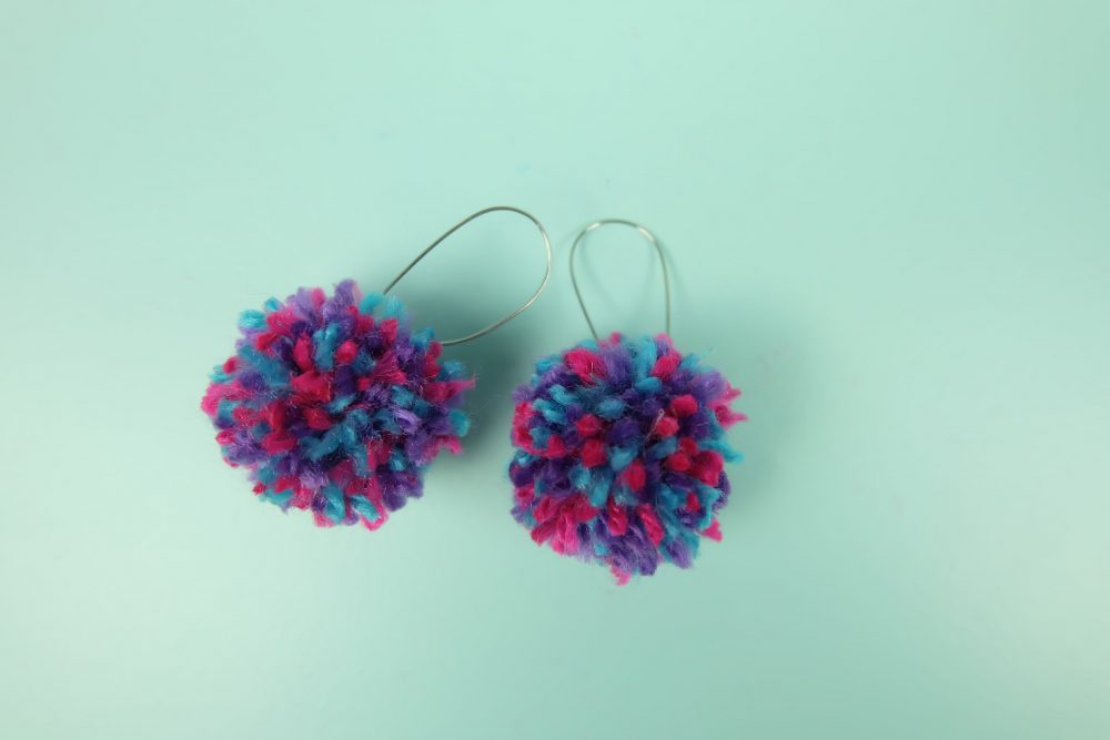 Learn how to make DIY Pom Pom Earrings in minutes with this quick and easy tutorial! Make an adorable pair of earrings to match any outfit! Also learn how to make a DIY pom pom maker in any size using a piece of cardboard! This would make an adorable handmade gift for teens or tweens! #DIY #Craft #pompoms #Earrings