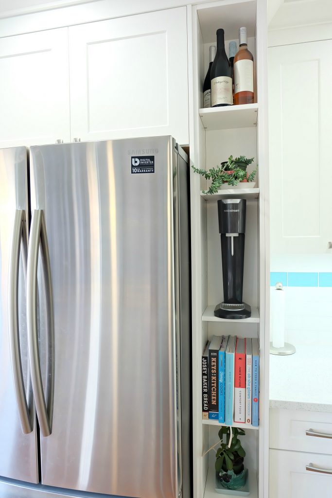 A shelf for cookbooks, wine and a soda stream hides pipes and plumbing from being in plain view! Hello Creative Family selected a palette of white, grey, teal, turquoise and aqua for their kitchen renovation! This DIY aqua kitchen remodel includes a colorful island and other smart features. Also check out her 20 Tips for a Smooth Kitchen Renovation! #Sponsored #Turquoise #Kitchen #Aqua #KitchenRemodel #kitchenrenovation