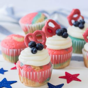 Celebrate the Fourth of July with this Patriotic Cupcakes Recipe! With red, white and blue swirls, buttercream frosting, hand dipped candy coated pretzels and blueberries, this is a fun Fourth of July Cupcake decorating idea! Great for other patriotic holidays too! Who doesnt love red, white and blue food ideas! #Cupcakes #FourthOfJuly #Patriotic #Baking #CupcakeDecorating #Recipe #CupcakeRecipe #RedWhiteAndBlue #PatrioticFood