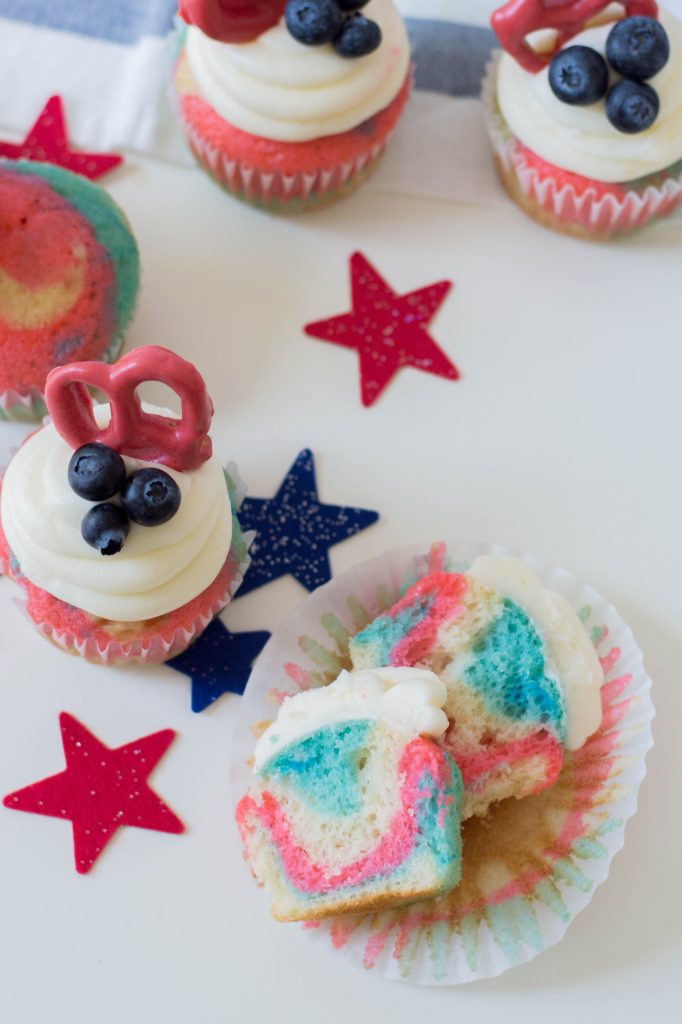 Celebrate the Fourth of July with this Patriotic Cupcakes Recipe! With red, white and blue swirls, buttercream frosting, hand dipped candy coated pretzels and blueberries, this is a fun Fourth of July Cupcake decorating idea! Great for other patriotic holidays too! Who doesn't love red, white and blue food ideas! #Cupcakes #FourthOfJuly #Patriotic #Baking #CupcakeDecorating #Recipe #CupcakeRecipe #RedWhiteAndBlue #PatrioticFood