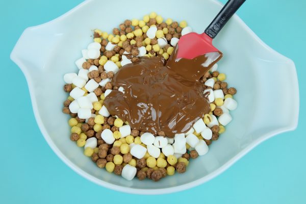 Pouring chocolate peanut butter mixture over cereal mix.