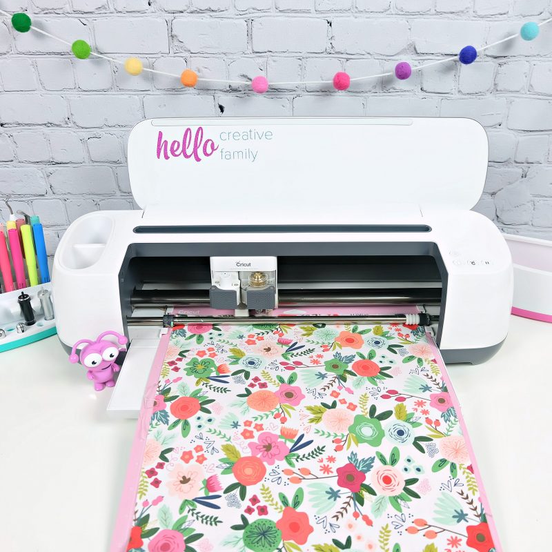 Cricut Maker loaded with a fabric mat with pretty floral fabric. A Cricut cutie sits next to the Cricut Maker.