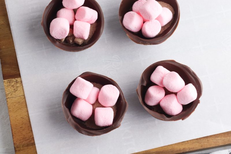 When the chocolate is set, remove each of the chocolate pieces from the mold. Add a small amount of instant hot cocoa mix to half the pieces and top the hot cocoa mix with marshmallows and half the sprinkles.