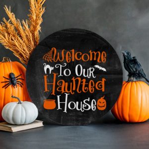 Round Welcome To Our Haunted House sign next to pumpkins and Halloween Decorations