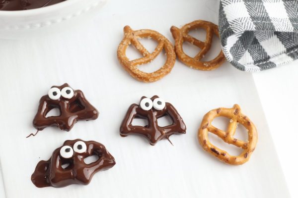 Transfer the covered pretzels to a piece of wax paper on a baking sheet. Place two candy eyes on the top of the bat, then allow the chocolate to cool and set. You can put your baking sheet in the refrigerator to speed up this process.
