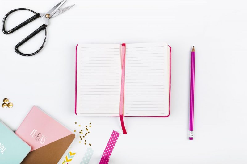 Pink journal on a desk with scissors, pencils and other office supplies