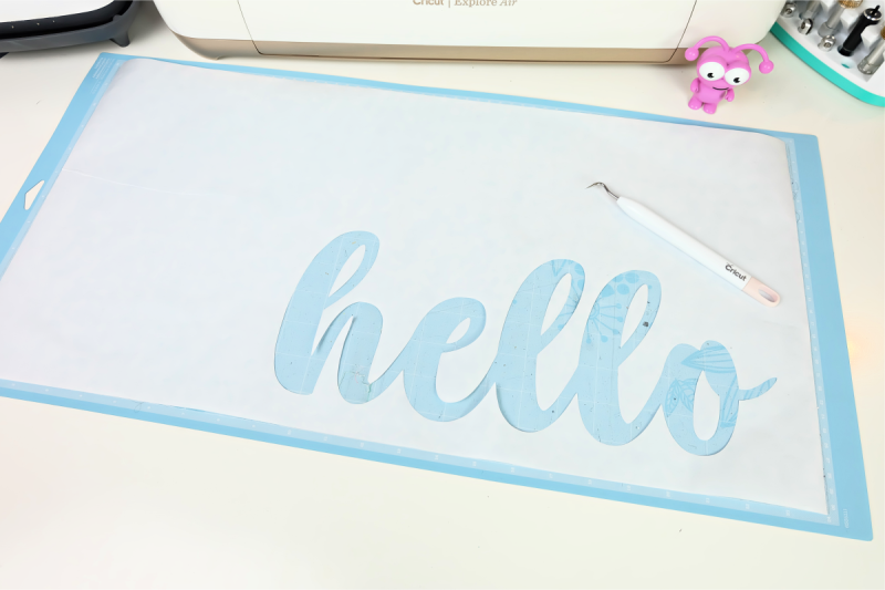 Weed your freezer paper. You will want to keep the freezer paper that surrounds the word as well as the pieces from inside the loops of the letters, so for my Hello design that meant the loops inside the h, e, l, l, o.