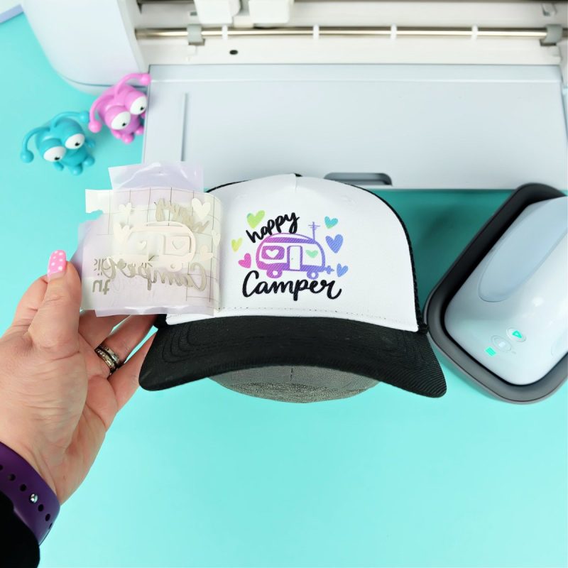 Peeling up Happy Camper Infusible Ink design off of a Cricut Hat