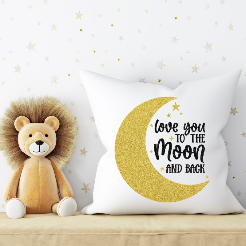 Pillow with a Love You To The Moon and Back Cricut design, sitting next to a stuffed lion in a children's room or nursery. 