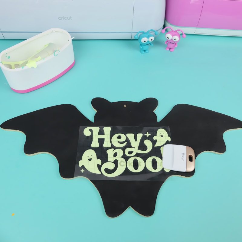 position your transfer tape where you would like the design to be. Run your scraper tool over top, pushing the vinyl against the wood. Peel away the transfer tape, leaving your design behind on your sign.