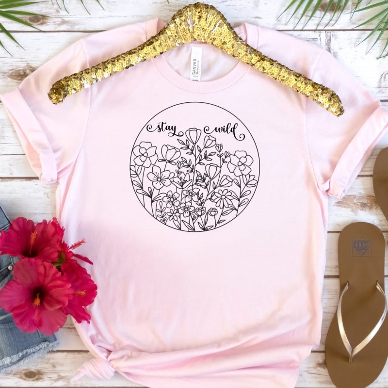 Pink t-shirt with a design with wildflowers in a circle with the words Stay Wild above.