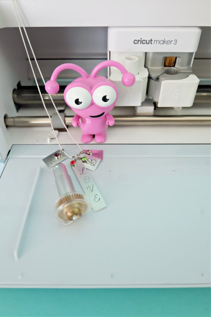 Engraved Cricut Keepsake Jewelry sitting on a Cricut Maker with a Cricut Cutie