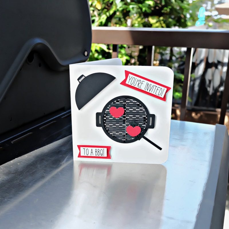 Cricut BBQ invitation sitting next to a BBQ.
