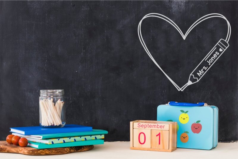 An image displaying a classroom chalkboard with a heart shaped decal on the chalkboard with a pencil and the teacher's name. This image represents the vibrant and creative learning environment of a classroom.