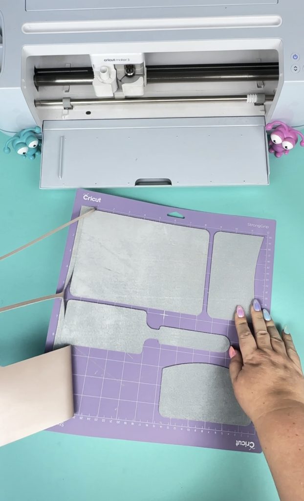 Cricut Maker 3 with a Cricut Strong grip mat and leather passport holder pieces cutout.