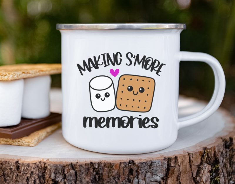 a white camping mug with the "Making S'more Memories" SVG design created by Crystal Allen from Hello Creative Family showcased on its surface. The design features an adorable Kawaii Marshmallow and Graham cracker surrounded by s'mores elements.