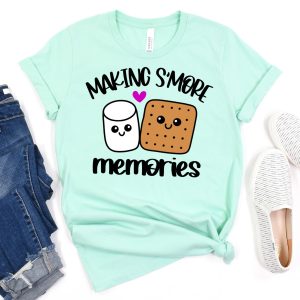 An image of a mint-colored shirt featuring the "Making S'more Memories" SVG design from Hello Creative Family. The design includes an adorable Kawaii Marshmallow and Graham cracker surrounded by s'mores elements.