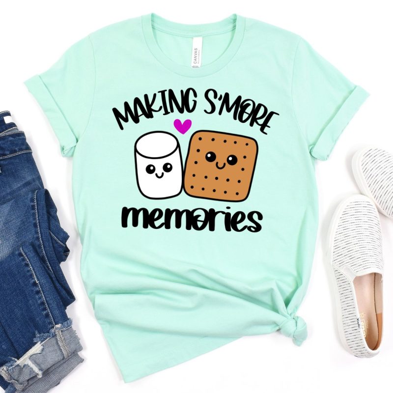 An image of a mint-colored shirt featuring the "Making S'more Memories" SVG design from Hello Creative Family. The design includes an adorable Kawaii Marshmallow and Graham cracker surrounded by s'mores elements.
