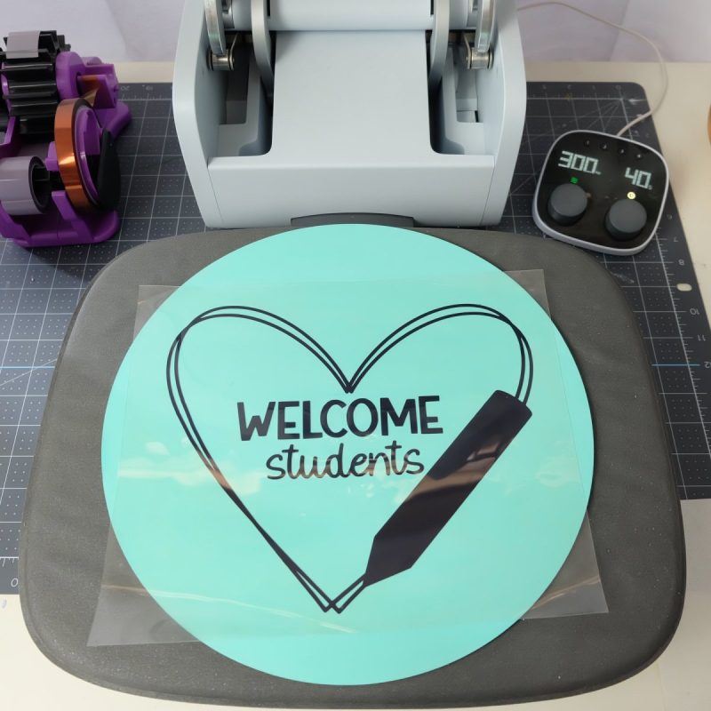 Wood sign laying on Cricut Autopress with welcome students design laying on top.