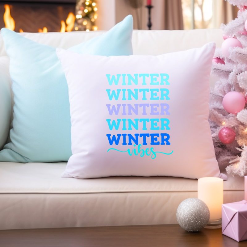 White throw pillow on a white couch with  white Christmas tree next to it. Pillow has Winter Vibes in pretty winter shades of blue on the front. 