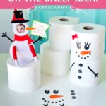 DIY Elf on the Shelf snowman scene featuring an elf in a snowman costume and snowmen made from toilet paper rolls with vinyl decals.