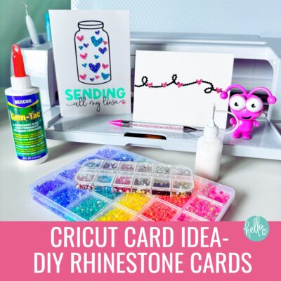 Two rhinestone cards sitting in front a a Cricut Maker 3 with supplies for making rhinestone cards
