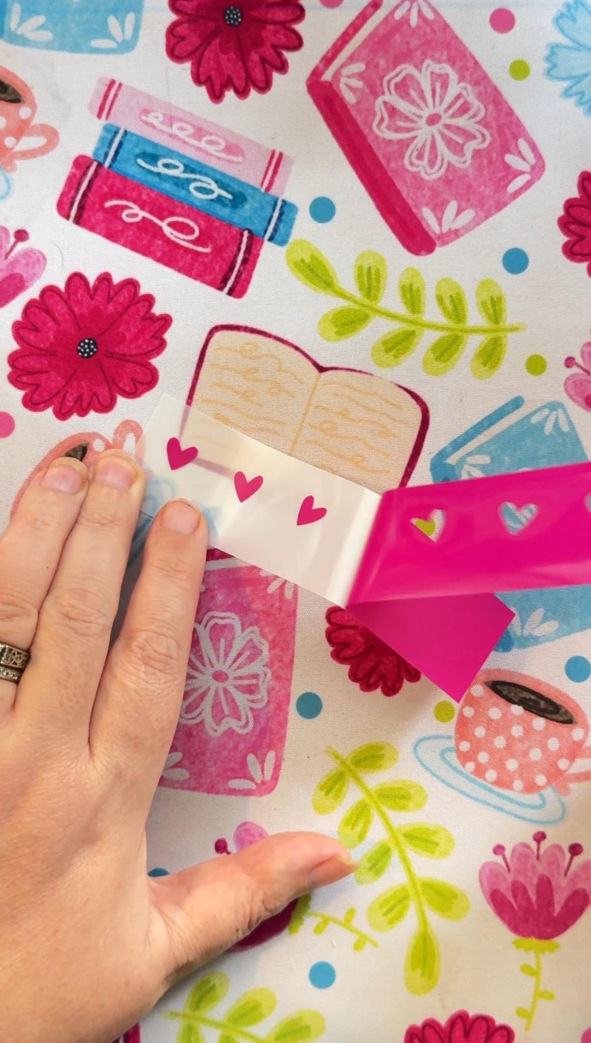 Hands weeding pink vinyl revealing hearts on the paper backing