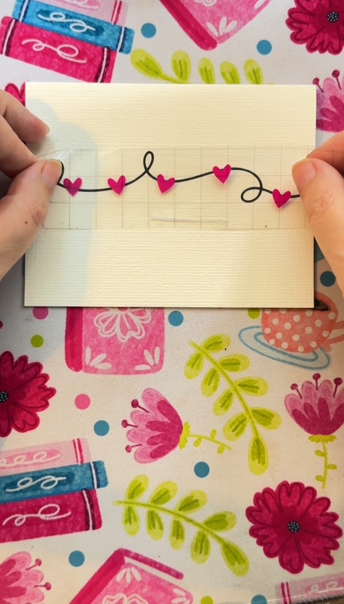 Hands using transfer tape to transfer pink hearts to the front of a greeting card