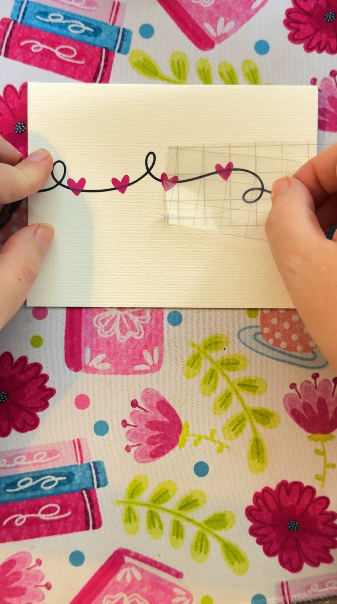 Hands using transfer tape to transfer pink hearts to the front of a greeting card