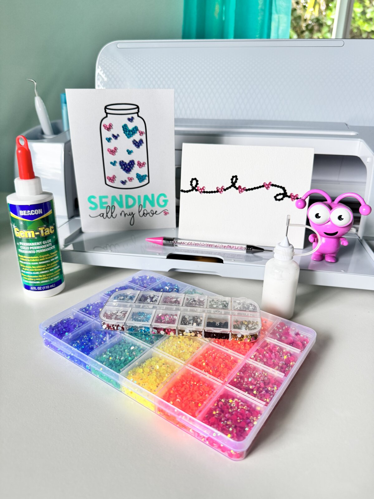 Two rhinestone cards sitting in front a a Cricut Maker 3 with supplies for making rhinestone cards