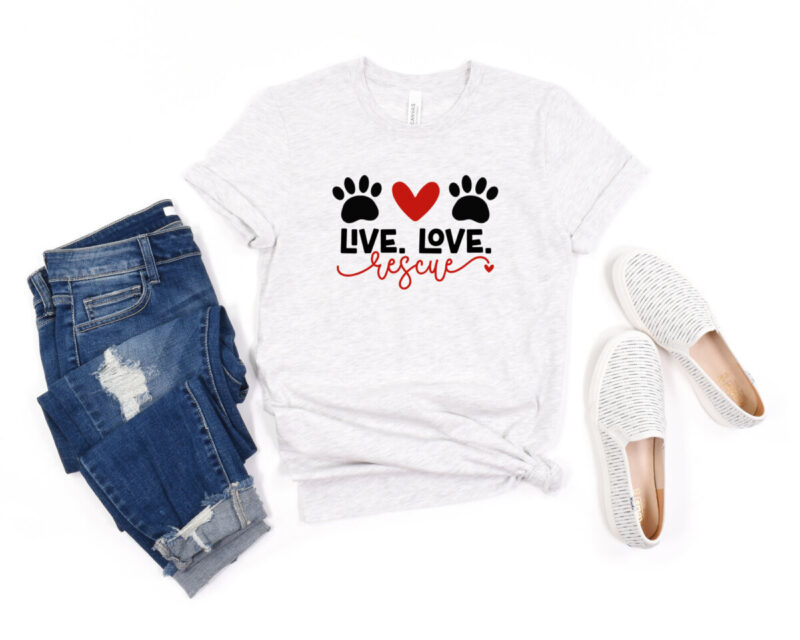 Shirt that reads Live Love Rescue with two paw prints and a heart. Shirt is laying flat with a pair of jeans and white slip on shoes next to it.