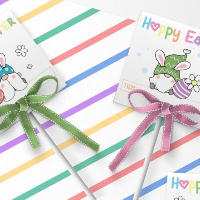 Easter Basket Printable: Free Printable Easter Tags for Lollipops- Adorable Easter Gnome Lollipop Covers with lollipops laying on top of piece of scrapbook paper with pastel stripes.
