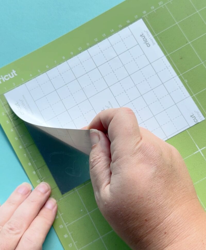 Carefully peel off the vinyl backing, leaving the design stuck to the transfer tape. If any pieces of your vinyl lift you may want to use your scraper tool or weeding tool to push them down onto the transfer tape. You may notice as you peel up the vinyl backing that some "Pre-weeding is done for you and pieces that you would be removing stay behind on the vinyl backing. This is 100% ok, just double check that no pieces you need are being left on the backing.