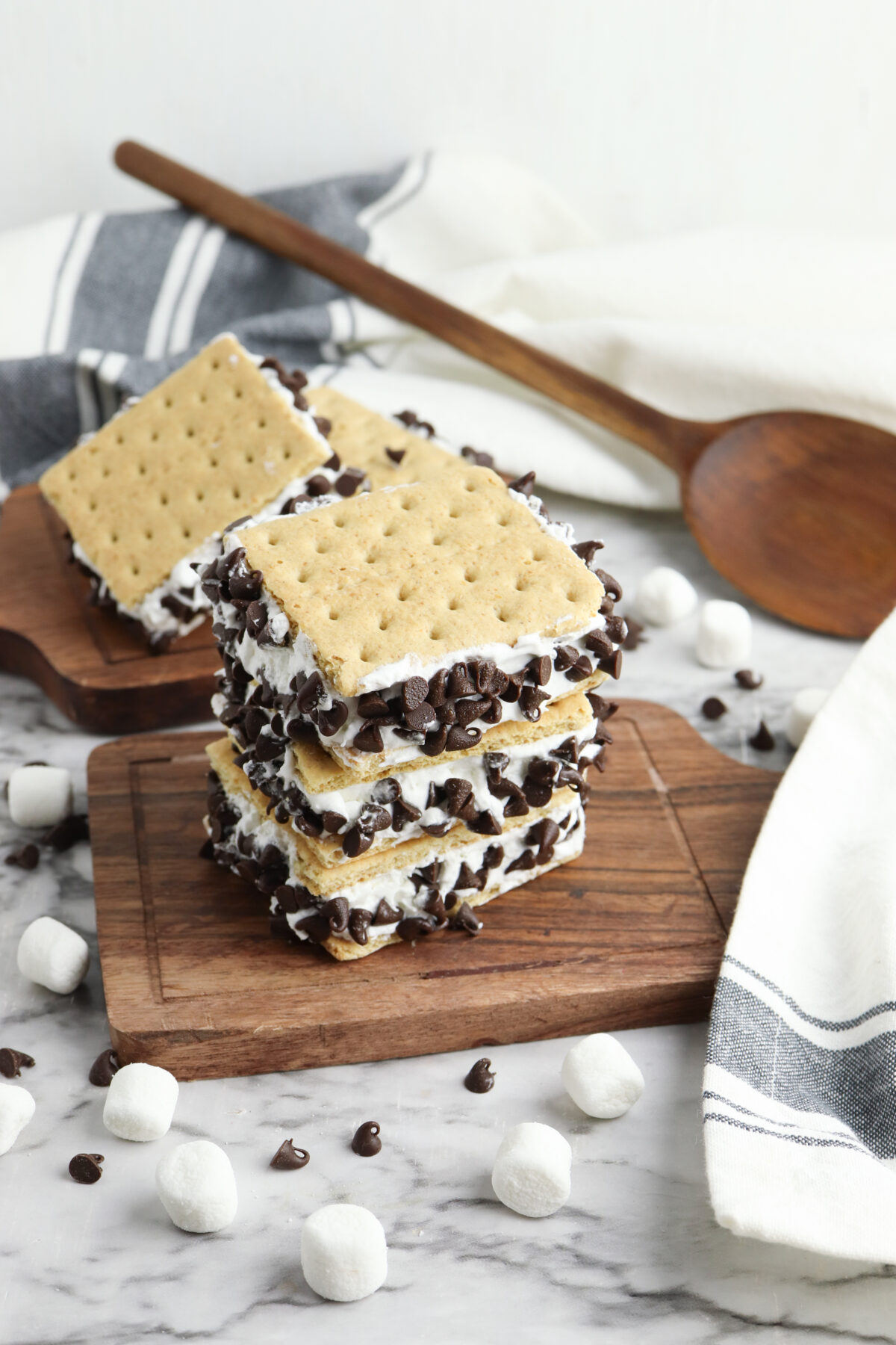 Homemade Frozen Smores sitting on a cutting board surrounded by marshmallows and chocolate chips.